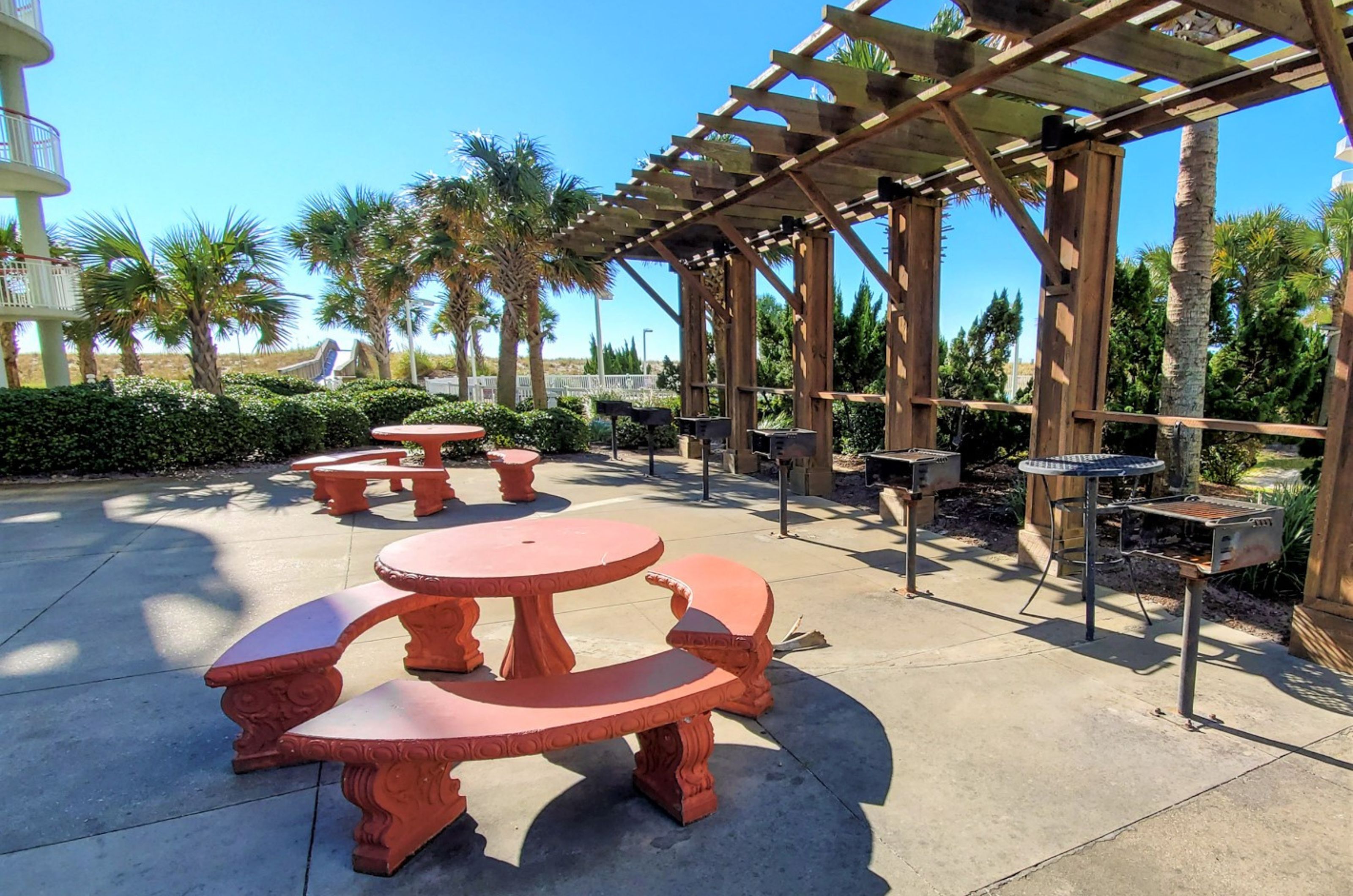 Red picnic tables on an outdoor patio next to multiple charcoal grills 