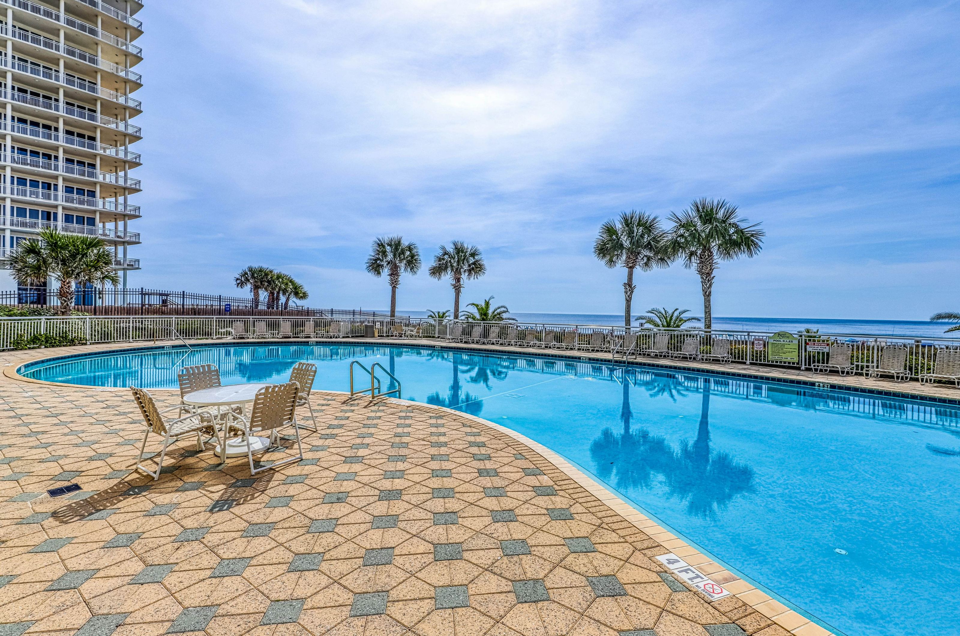 Large outdoor swimming pool and deck next to the Gulf of Mexico and Beach Colony Resort high-rise 