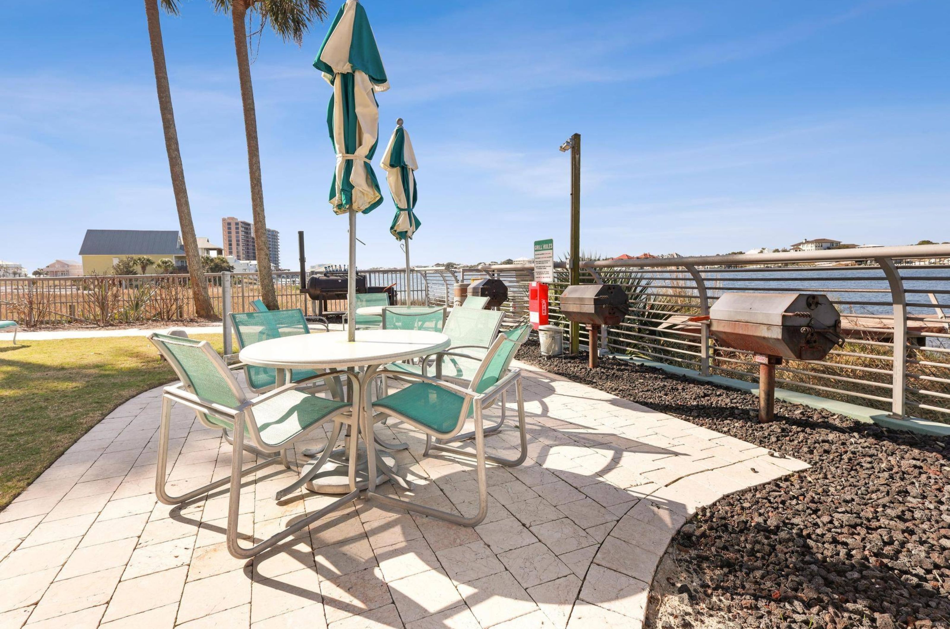 One outdoor dining table and barbecue grills on a deck next to the water 