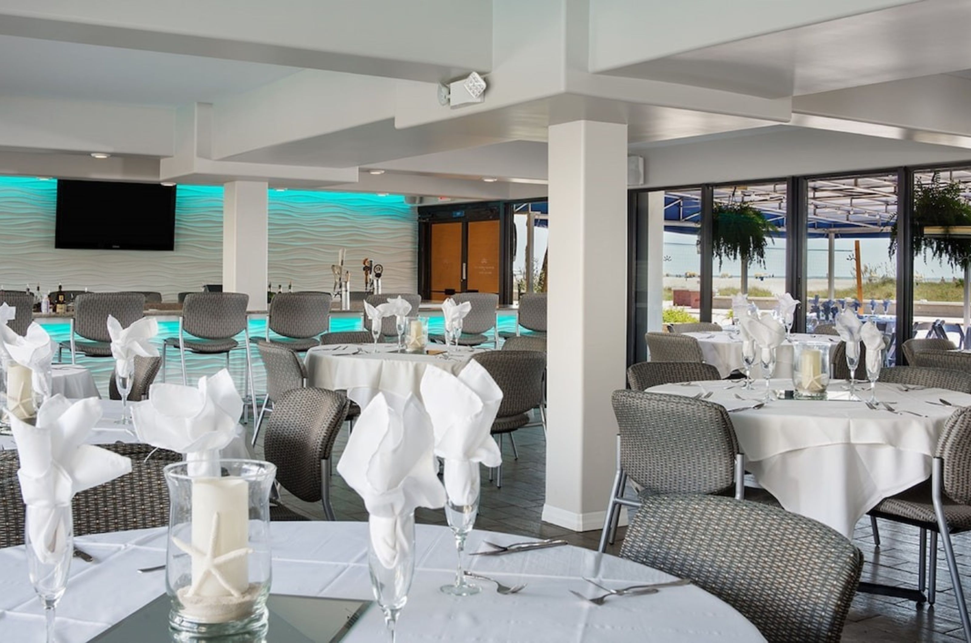 Elegant tables next to beach-facing windows and the bar in the event space at Bilmar Beach Resort 