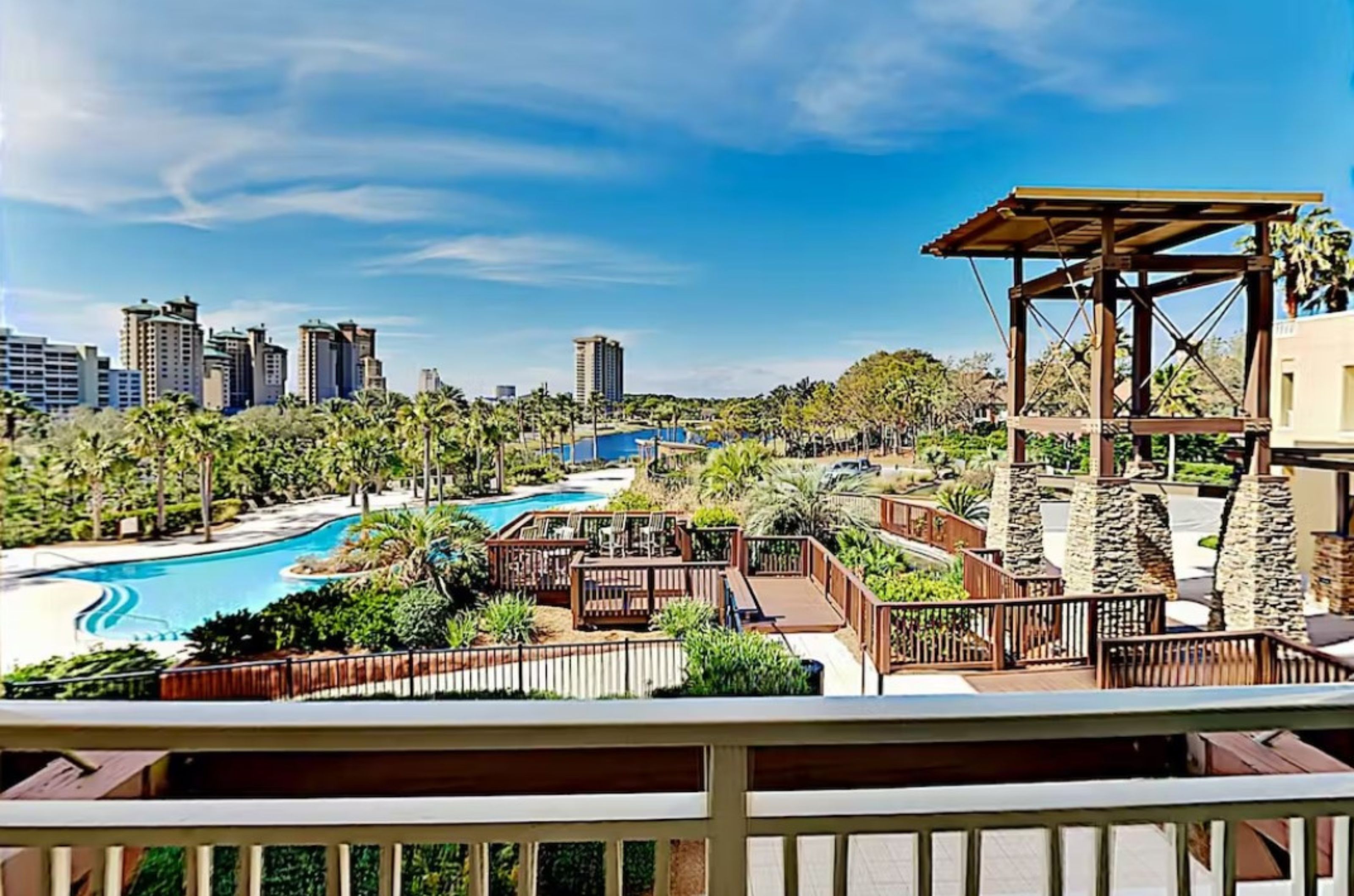 The winding lagoon pool nestled between a spacious wooden deck with seating in the foreground and a deep-blue lake in the distance