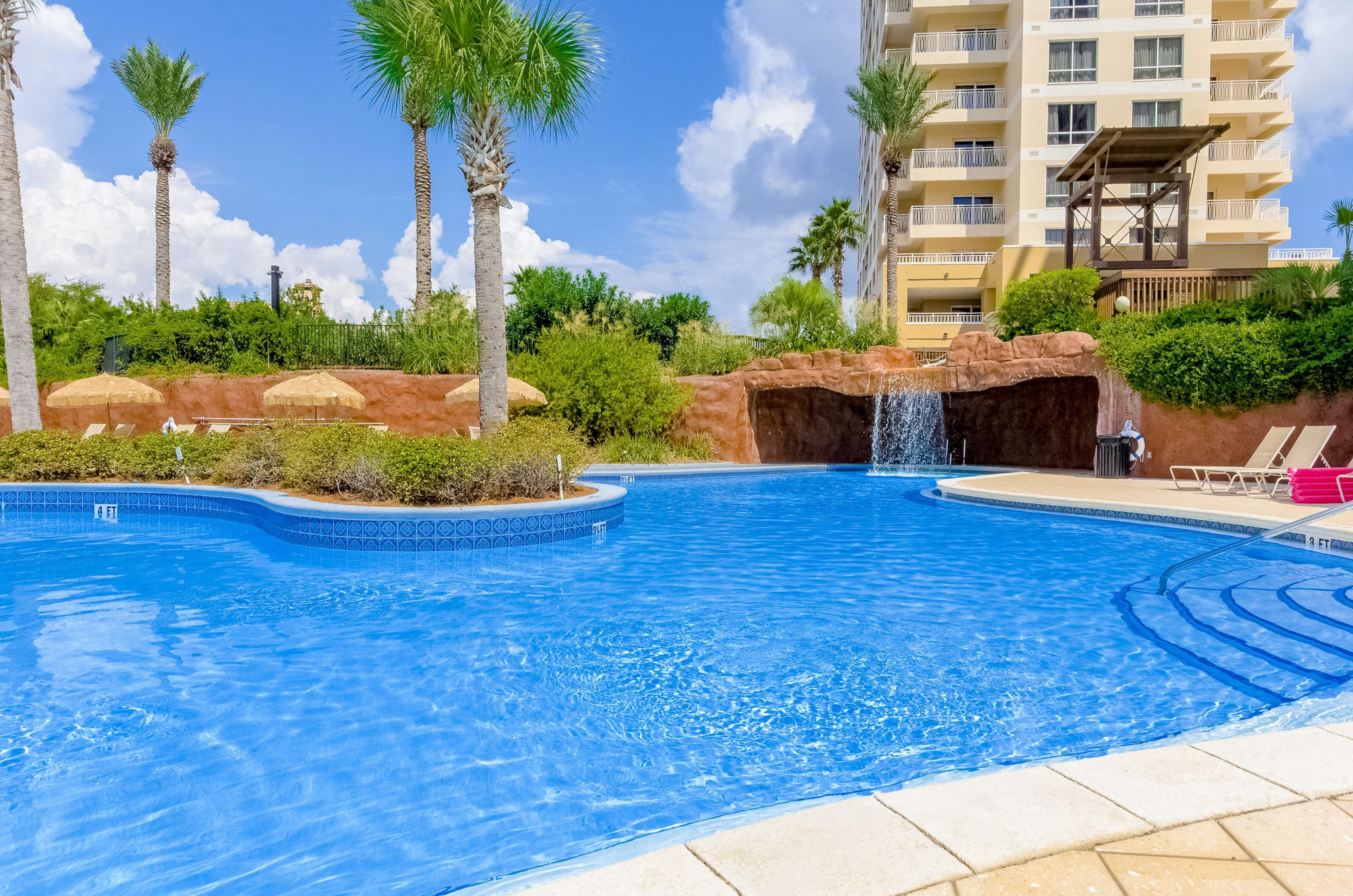 The shimmering aqua pool winds into a cave with a waterfall at the entrance and has loungers and tiki umbrellas on the sundeck