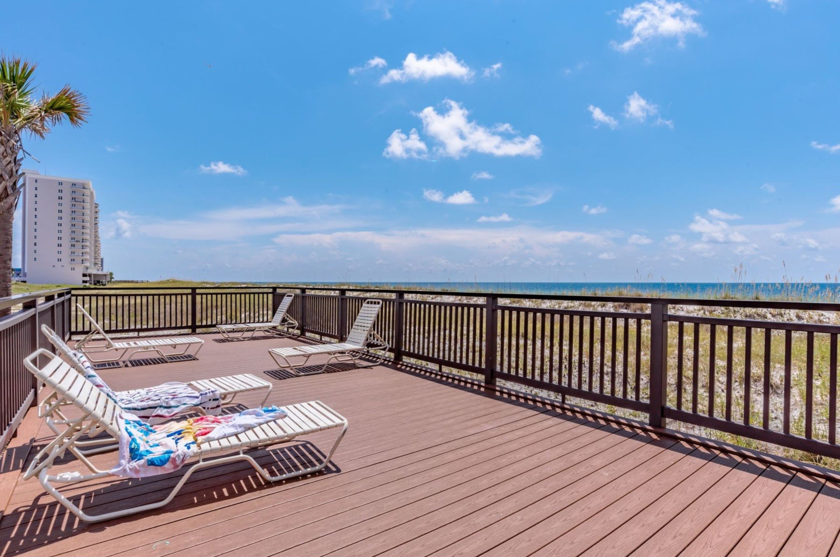 A deck by the beach with lounge chairs overlooking the Gulf 