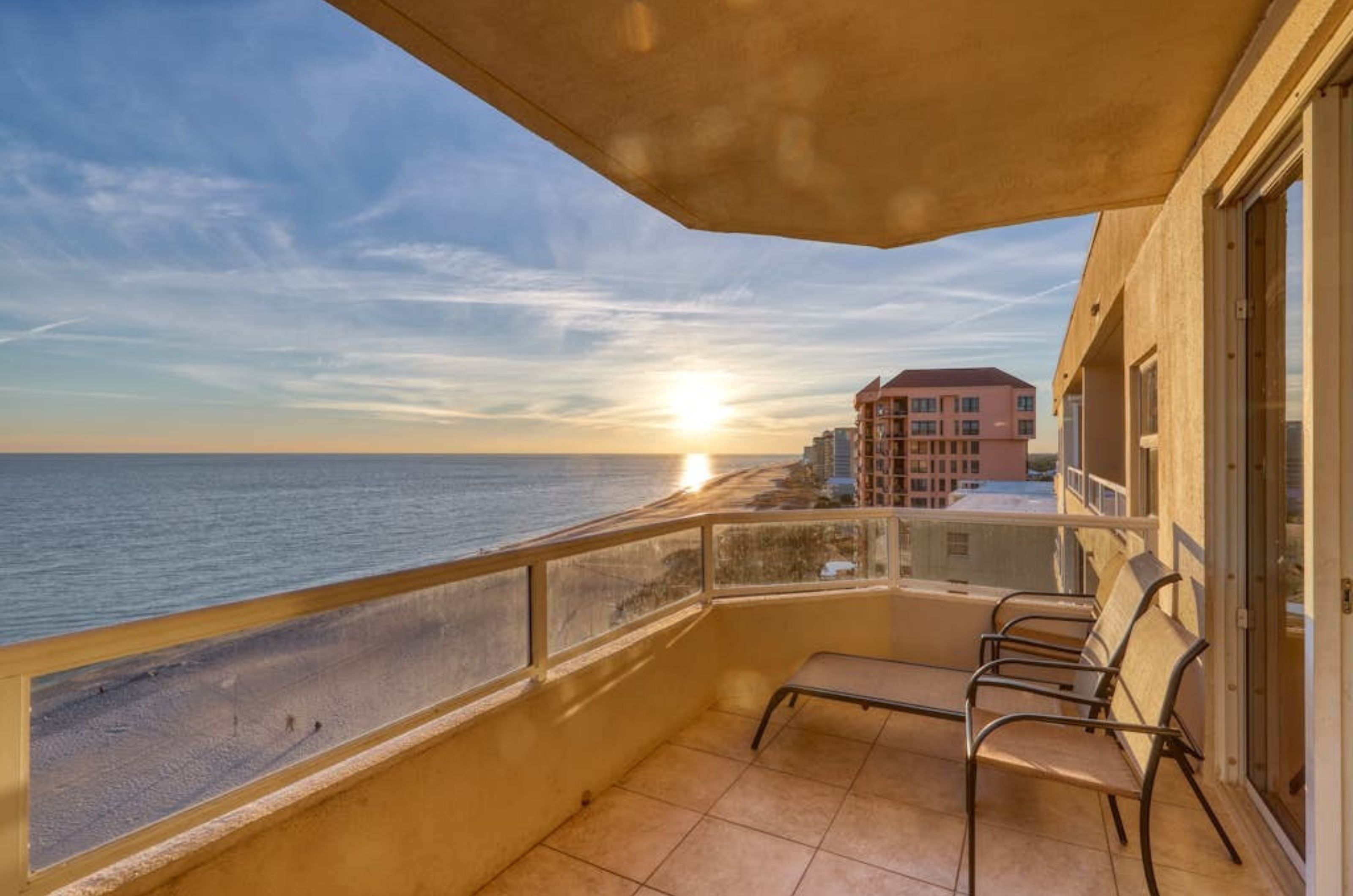 A lounge chair on a private balcony overlooking the beach at sunset at the Enclave 